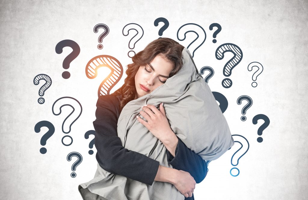 Eine Frau hält ein großes Kissen umarmt, die Augen sind geschlossen. Sie wirkt erschöpft, und um sie herum sind gezeichnete Fragezeichen, was Verwirrung symbolisieren könnte.