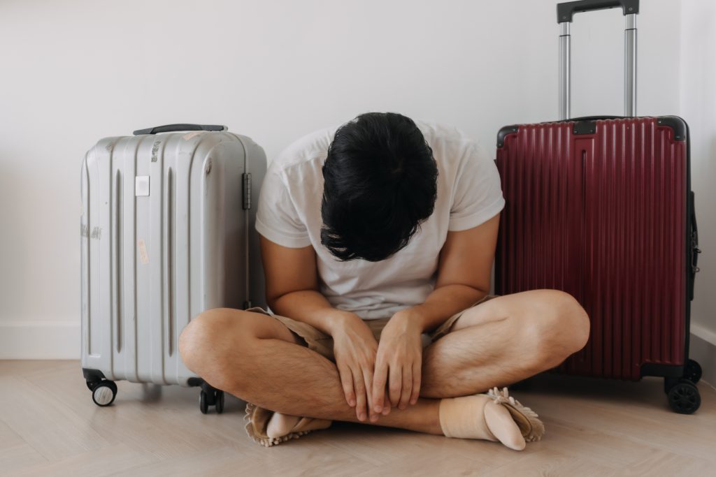 Mann sitzt erschöpft auf dem Boden neben Koffern. Dieses Bild zeigt typische Anzeichen von Jetlag nach einer langen Reise über mehrere Zeitzonen.