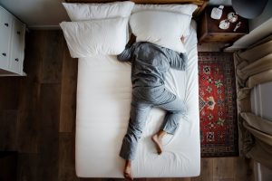 ine Person liegt auf einem Bett, verdeckt den Kopf mit einem Kissen, vermutlich wegen störendem Lärm.