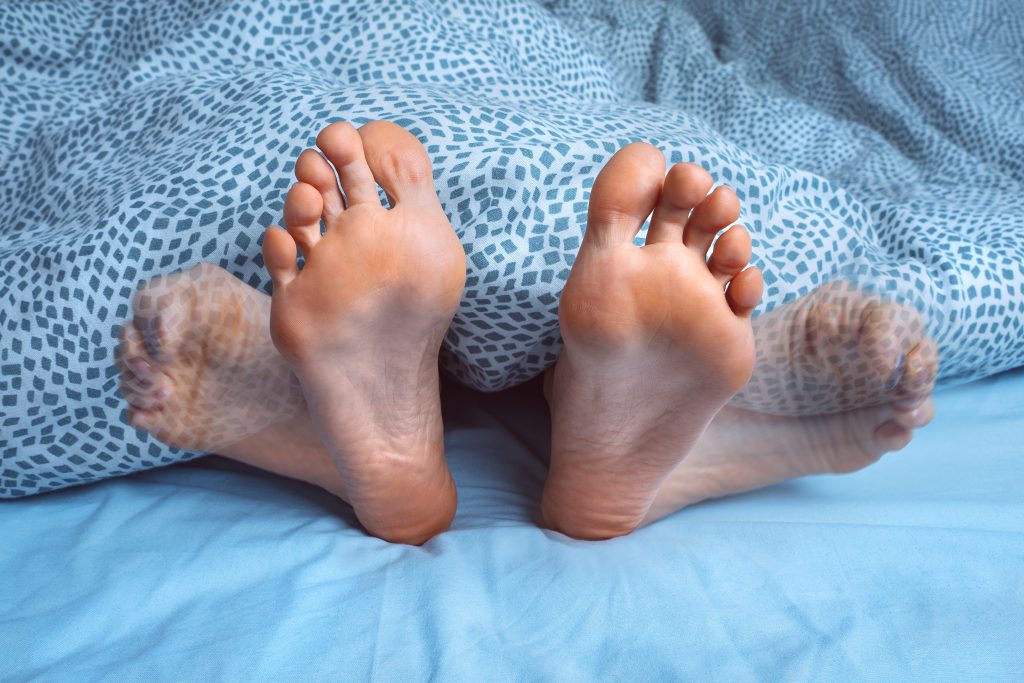 Beine in Bewegung unter einer Decke, typisch für das Restless-Legs-Syndrom während der Nacht.