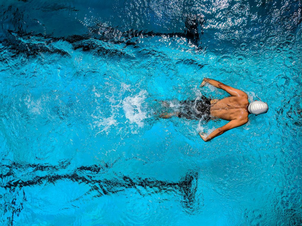Ein Schwimmer in einem blauen Pool, der einen kraftvollen Schwimmzug ausführt – ein Beispiel für moderates Ausdauertraining, das nachweislich die Schlafqualität verbessern kann.