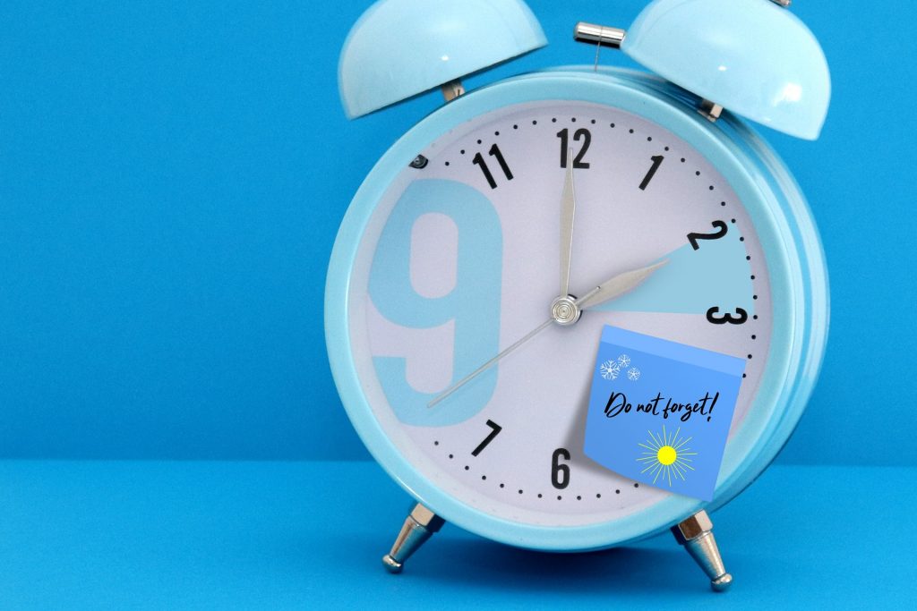 Ein hellblauer Wecker mit einer Notiz erinnert an die Umstellung auf die Sommerzeit. Die Zeitumstellung beeinflusst den Schlaf-Wach-Rhythmus und kann unsere innere Uhr aus dem Takt bringen.