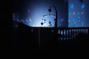 Ein Kinderzimmer bei Nacht, beleuchtet von einem Sternenhimmel-Projektor über einem Babybett. Die Szene vermittelt eine beruhigende Schlafumgebung für Babys.