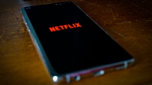 Ein Smartphone zeigt das Netflix-Logo auf einem dunklen Holzuntergrund, was die Ablenkung durch Streaming-Dienste vor dem Schlafengehen symbolisiert.