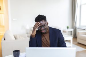 Ein müder Mann sitzt mit der Hand auf der Stirn vor seinem Laptop. Dieses Bild symbolisiert die Auswirkungen hormoneller Ungleichgewichte, die Müdigkeit und Konzentrationsprobleme verursachen können. Erfahren Sie auf sleeplab.ch mehr über hormonelle Ursachen von Schlafstörungen in der Schweiz.