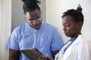 Zwei medizinische Fachkräfte in blauer und weißer Kleidung besprechen Patientendaten auf einem Tablet. Eine präzise Diagnose ist entscheidend, um Risikofaktoren wie Schlafapnoe und deren Auswirkungen auf das Schlaganfallrisiko frühzeitig zu erkennen.